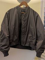 Front view of olive bomber jacket on hanger showing overall style, color and zipper