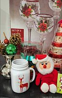 Group shot showing boxed candle holders, mug, Santa plush, vase pick and ornament set