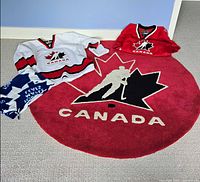 Full view of red Hockey Canada rug with both jerseys and scarf displayed
