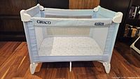 Front angled view showing overall playard structure, branding, mesh sides and mattress insert