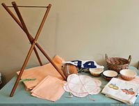 All items grouped on table including wooden stand, placemats, napkins, bowls, basket, doily, fruit cloth