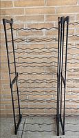 Full view of one black metal wine rack showing nine wavy bottle tiers