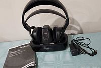 Headphones on charging base with manual and power adapter visible