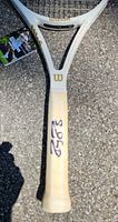 Close-up of autographed Wilson racquet handle, beige grip, visible signature, tag hanging