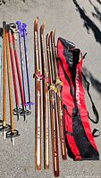 Full view of two pairs skis, four pairs poles and Salomon bag on ground