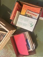 Box with multiple songbooks including Bradley’s Carols and Songs for the Christmas Season and loose music sheets