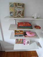Shelving unit with blanket (not visible here) and multiple children’s books, pink cushion