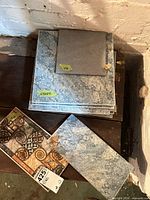 Stack of large gray stone-look tiles with smaller square and decorative piece visible