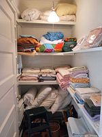 Shelves filled with folded linens, pillows, blankets, towels, wicker basket and vacuum visible