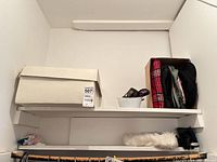 Shelf holding straw hat box, bowl with sunglasses, cardboard box with wool caps and scarf, faux-fur collar below