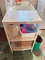 Utility sink stand with shelves, wastebasket partially visible