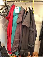 Multiple jackets on rail: red, teal, brown puffer, two black coats
