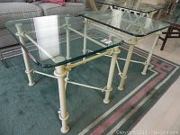 Pair of tables showing beveled glass tops and textured white wrought iron bases with tubular leg supports and connecting crossbars.