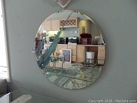 Clear full view of round wall mirror with beveled edge and applied art glass flare design mounted on a neutral wall.