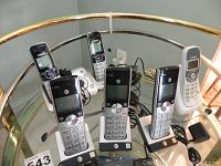 Five cordless phones, two VTech CS6423 models in front with bases, three white AT&T cordless phones with charging bases in back, cords visible on glass table.
