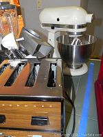 KitchenAid K45SS mixer with stainless steel mixing bowl and attachments alongside Farberware toaster with woodgrain front and chrome sides