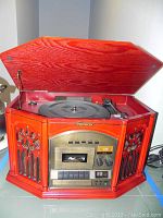 Front angled view with the lid opened revealing the turntable, cassette player, control buttons and speaker grille design.