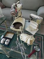Full lot overview showing Sunbeam Mixmaster mixer, electric can opener, Black & Decker hand mixer with beaters, and boxed Royal Worcester egg coddlers on glass table