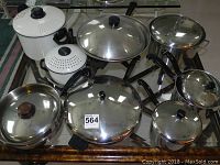 Full set of stainless steel pots, pans and electric wok displayed on glass table