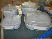 Four square Corningware bowls with clear glass lids, on table, all sizes visible
