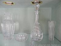 Multiple crystal items displayed in a glass cabinet shelf: Baccarat vase, Atlantis decanter and stopper, small bowl, and a tall vase.