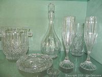 Baccarat crystal decanter with stopper, crystal ice bucket, two crystal flutes, and tall crystal vase shown together on shelf
