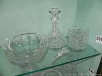 Photo showing the full set on a glass shelf: lobed bowl, decanter with stopper, and ice bucket.