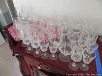 Photo showing the full collection of 34 crystal glassware pieces arranged on an ornate wood surface with a pink cloth underneath.