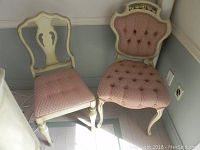 Front and side view of two vintage wooden chairs, one with tufted upholstery and decorative back, the other with shield backrest and patterned upholstered seat, both in cream finish and pink fabric.