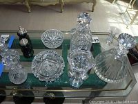 12 pieces of clear cut crystal serveware including decanters, candlesticks, ashtrays, and bowls with intricate designs, plus green Gucci salt and pepper shakers.