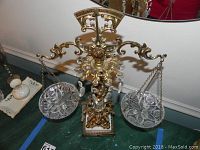 Front view of the bronzed ornate decorative scale with two hanging crystal dishes, showing the entire piece on a green floor.