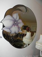 Front view of round mirror mounted on wall, shows flower design and reflection of room.