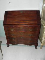 Front view of vintage mahogany secretary desk with closed top panel and ornate drawer handles.