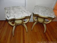 Pair of side tables with white and grey marble tops and gold-tone curving bases on hardwood floor.