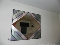 Full view of the square geometric mirror showing cool tone mirror segments and black bordering lines, hanging on a white wall