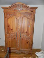 Full frontal image of the large wooden armoire showing floral carvings on doors and decorative curved top.