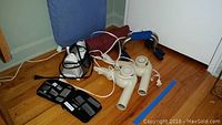 Photo showing two beige Conair hair dryers, a black Micro Touch Max personal hygiene kit, and black and blue exercise hand grips on a wooden floor.