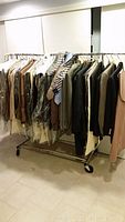 Rack with a variety of men's jackets, suits, and coats in plastic garment bags and hanging off rack, showing mix of browns, blacks, grays, and some patterned items, mostly size large.
