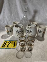 Group view of all items: two Vat 69 pitchers, four cups, decanter, four gold-rim shot glasses