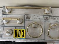 Five packaged brass and ceramic bathroom accessories displayed: towel bar, toilet paper holder, two towel rings, robe hook