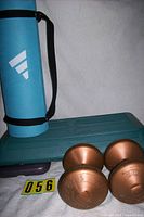 Overview of rolled blue yoga mat, teal aerobic step with purple risers, and pair of copper dumbbells