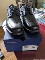 Front/top view of the pair of Rockport black leather dress shoes on their box