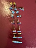 All cufflink sets and tie clips arranged vertically on red surface