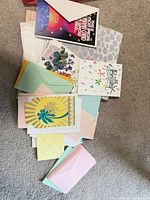 stack of assorted greeting cards and pastel envelopes spread on carpet
