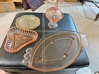 Four glass pieces grouped: pink oval tray, pink heart dish, pink covered candy dish, amber plate