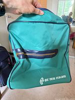 Front view of teal Air New Zealand carry-on bag showing logo and front zip pocket