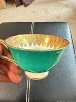 Side view showing green exterior, gold handle trim, footed base