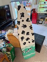 Full view of ironing board upright showing cow print cover and blue frame