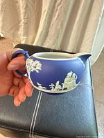 Side view showing cobalt blue creamer with white relief figures and handle