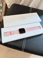 Top view of smartwatch in open box showing pink strap and rose-gold case